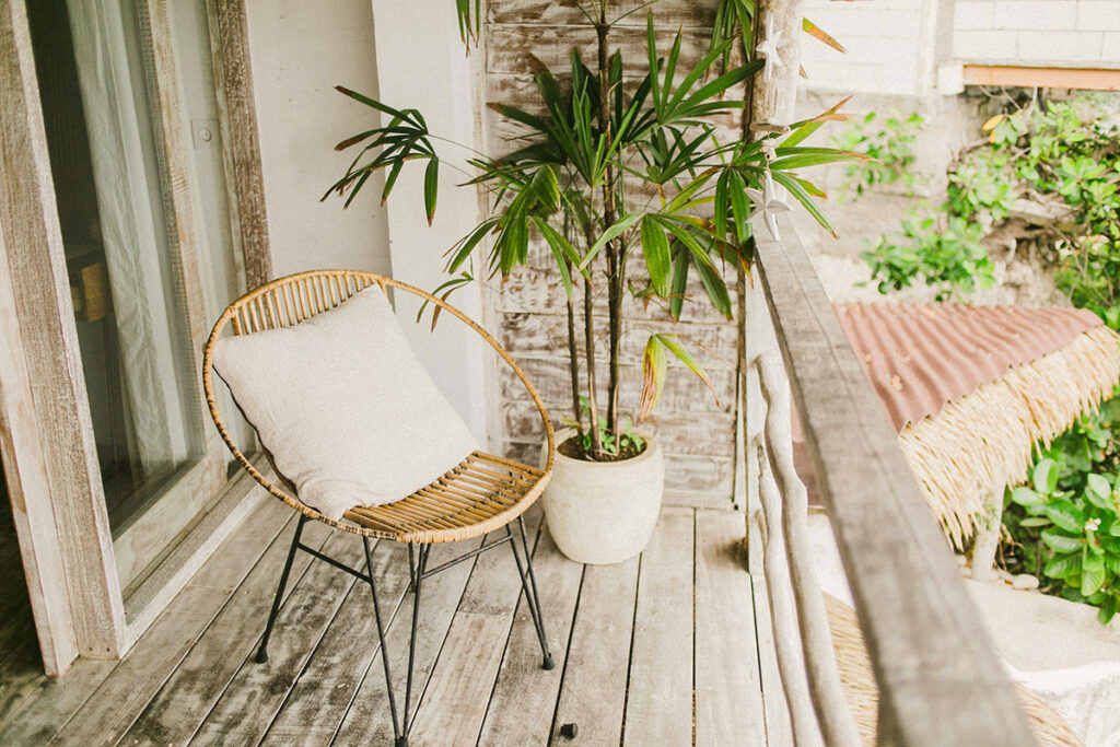 Small rustic balcony with a rattan circular chair, a throw pillow, and a tropical potted plant.