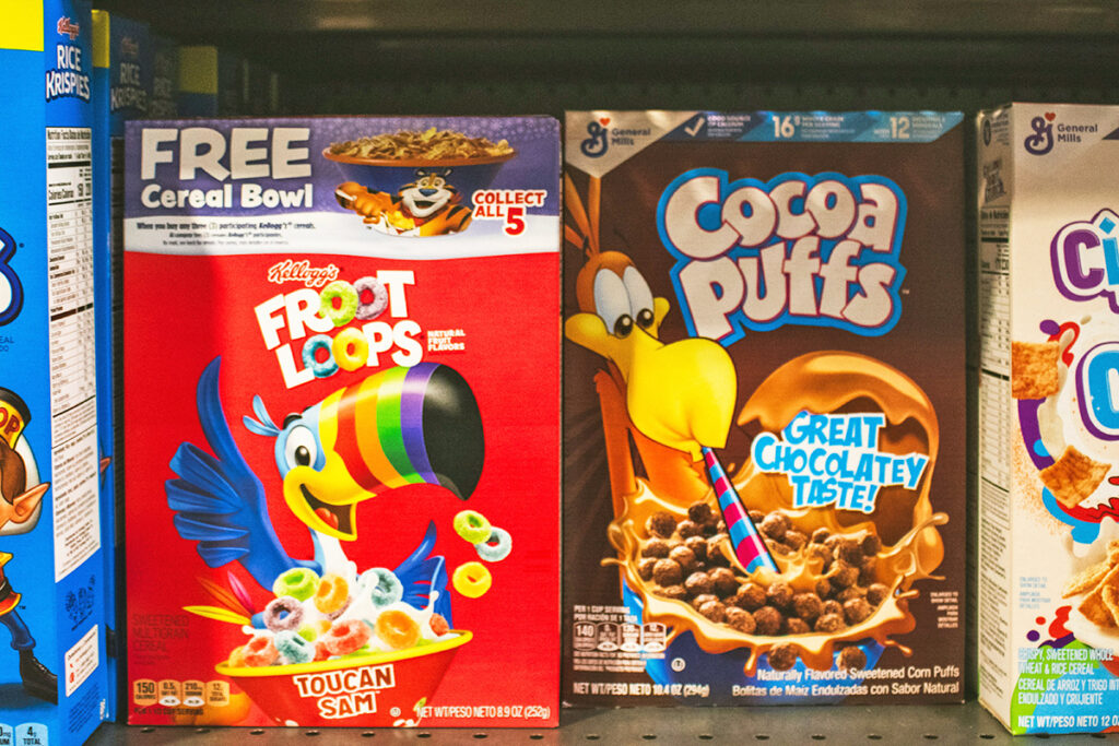 A grocery store shelf containing different brands of cereal in boxes, including Froot Loops, Cocoa Puffs, and Cinnamon Toast Crunch.