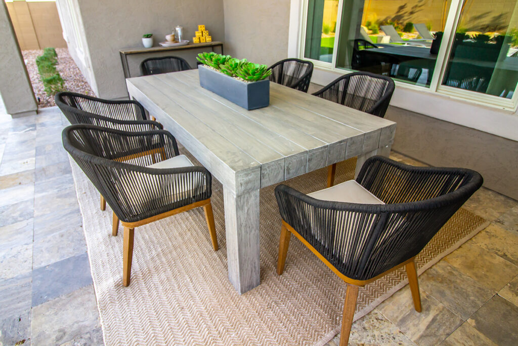 An outdoor dining table on a covered patio with a jute rug underneath.