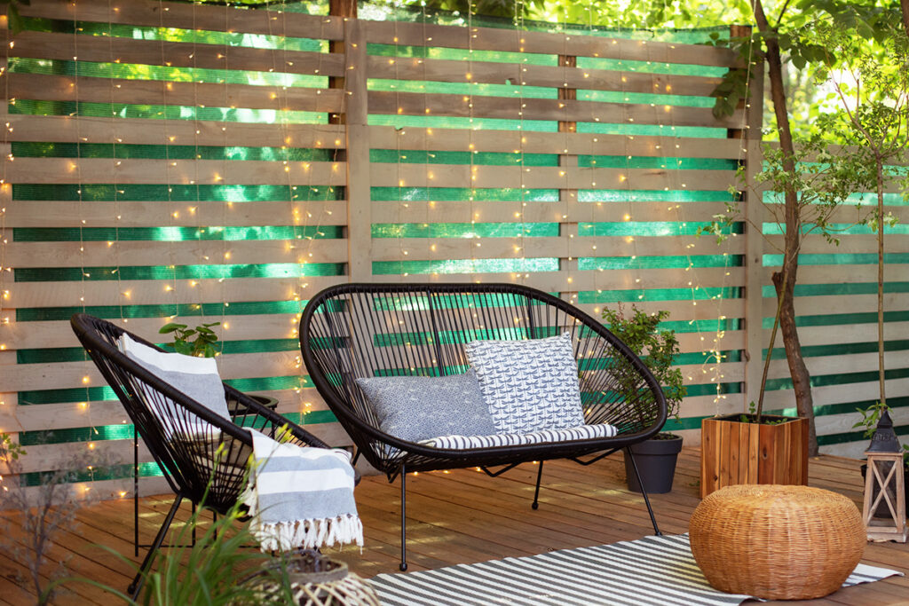 An outdoor seating area against a slatted privacy fence with cascading curtain lights behind it.