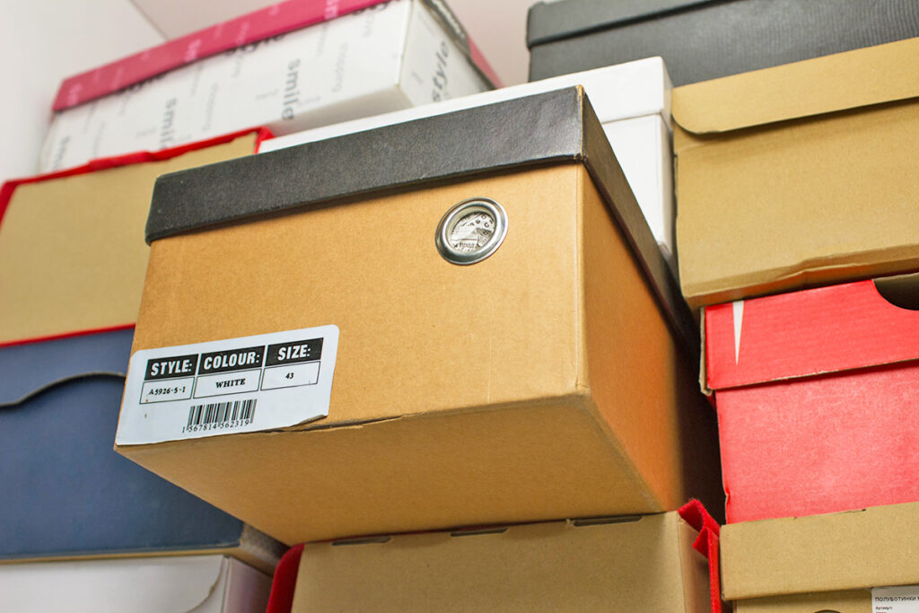 A stack of shoe boxes that appear to be store on the top shelf of a closet.