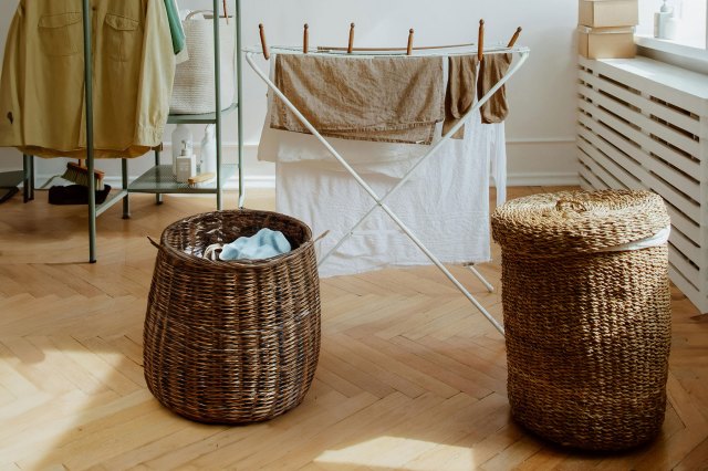 Two different wicked laundry baskets in the foreground and a clothes drying rack with linens on it in the background.