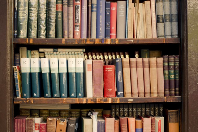 Close-up shot of an academic bookshelf. The bottom two shelves (three are pictured) each feature two layers of books. The back layer of books is slightly higher than the front for visibility.