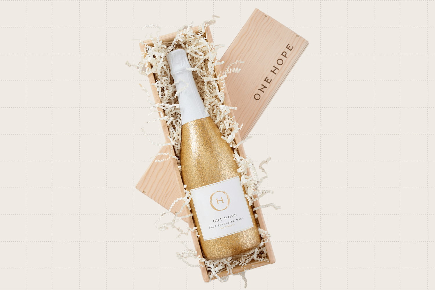 The Single Bottle Wood Gift Box from ONEHOPE. The bottle of brut sparkling wine has a gold and sparkly wrap. The wooden box it's in is filled with crimped paper filling.