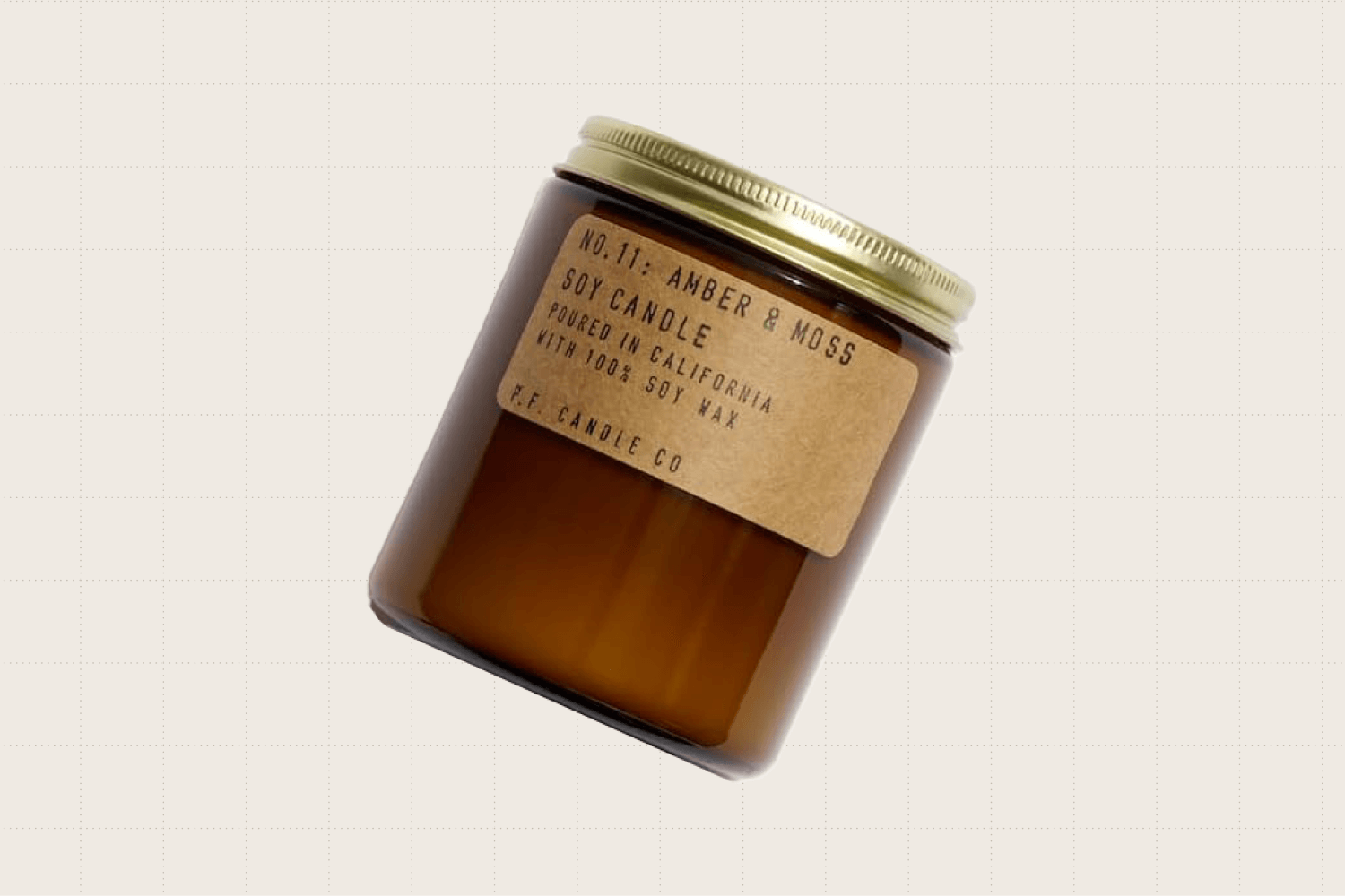 A P.F. Candle Co. candle in scent "Amber & Moss" shown in its transparent amber jar with a gold lid.