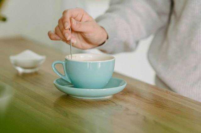 Anonymous person using a spoon to stir coffee in an aqua-colored cup on a matching saucer.