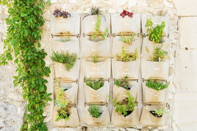 Over-the-door shoe organizer being used as a vertical planter for herbs. It's in an outdoor space and the pockets are labeled with the name of each herb.