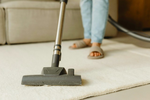 Anonymous person vacuuming a white area rug with a canister vacuum.