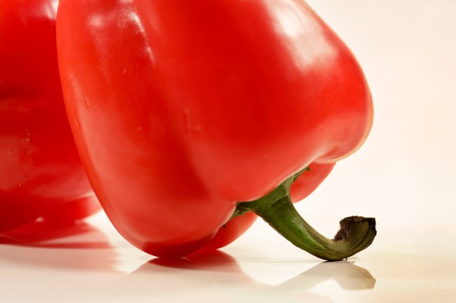 Close up of two red bell peppers upside down, stem-down on a flat surface.