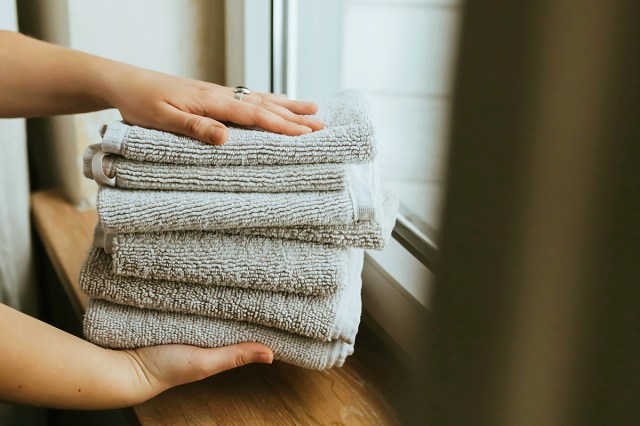 Anonymous person holding a stack of gray hand towels near a window.