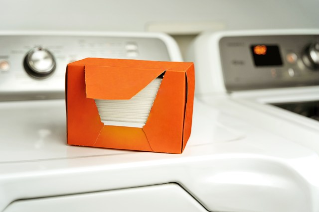 An orange cardboard box containing dryer sheets that's sitting on top of a dryer in a laundry room.