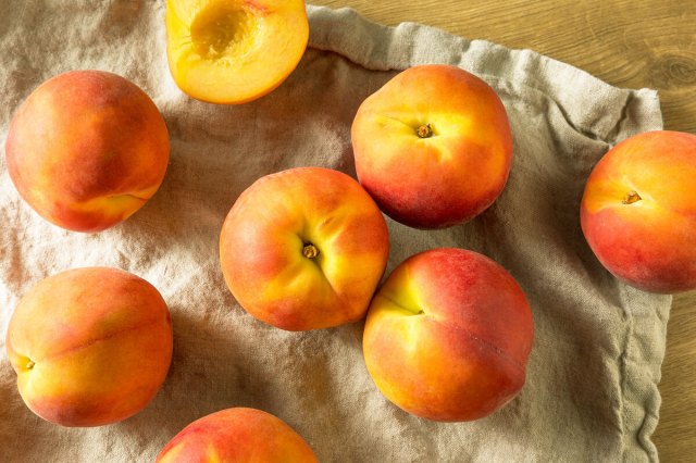 Close up of nectarines on a linen cloth. One of the nectarines is cut and half and shown without the pit.