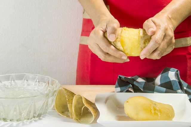 Anonymous person peeling two halves of a potato skin off effortlessly after boiling them whole.