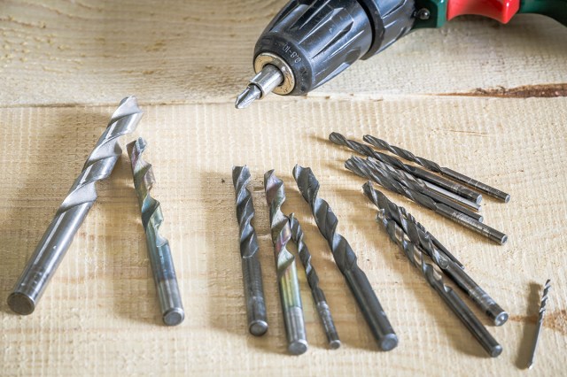 A drill laying on a wood surface surrounded by different size drill bits.