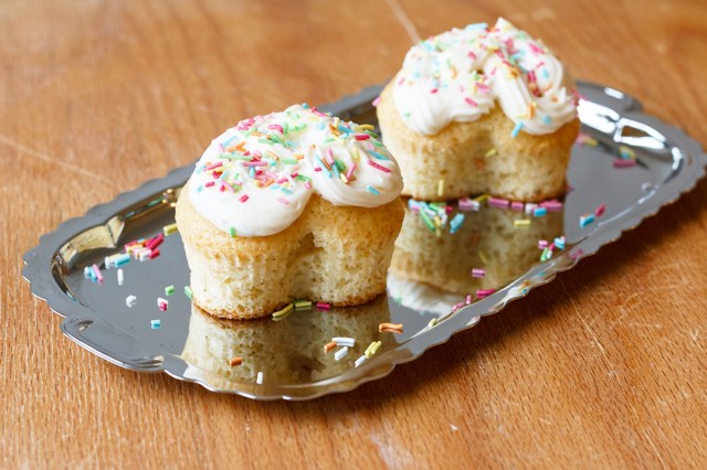 Two heart-shaped vanilla cupcakes sitting on a silver tray. They are topped with white frosting and colorful sprinkles.