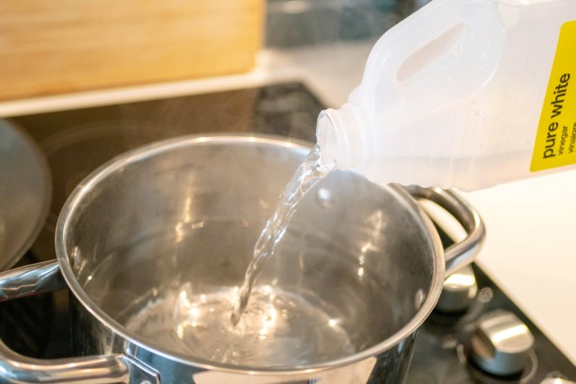 Anonymous person pouring distilled white vinegar into a saucepan on the stovetop.