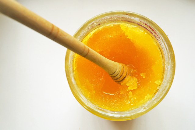 A glass jar of crystallized honey photographed from above. There is a wooden honey dipper in the jar to show the thick consistency of the honey.