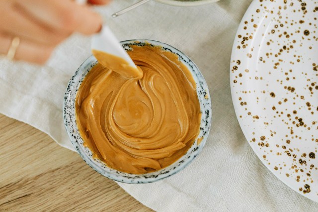 An anonymous person stirring a jar of peanut butter with a white plastic knife. The photo is shot from above.