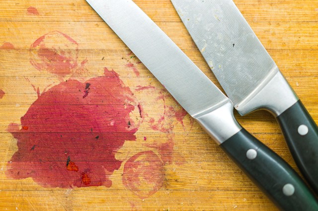 Close-up of a wooden cutting board with pinkish-red stains from beets. On the cutting board are two stainless steel knives.