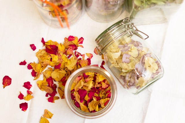 An open glass jar of potpourri shot from above. The floral petals are yellow and red. Next to it is a sealed glass jar on its side that's full of yellow and purple petals.