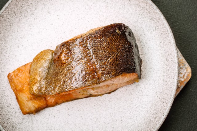 A cooked piece of salmon, skin-side up on a speckled dinner plate. The skin looks crispy and the fish is cooked through.