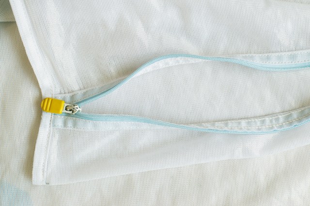 Close-up shot of a mesh laundry bag with an open zipper. The bag is lying flat on a surface and currently has nothing inside of it.